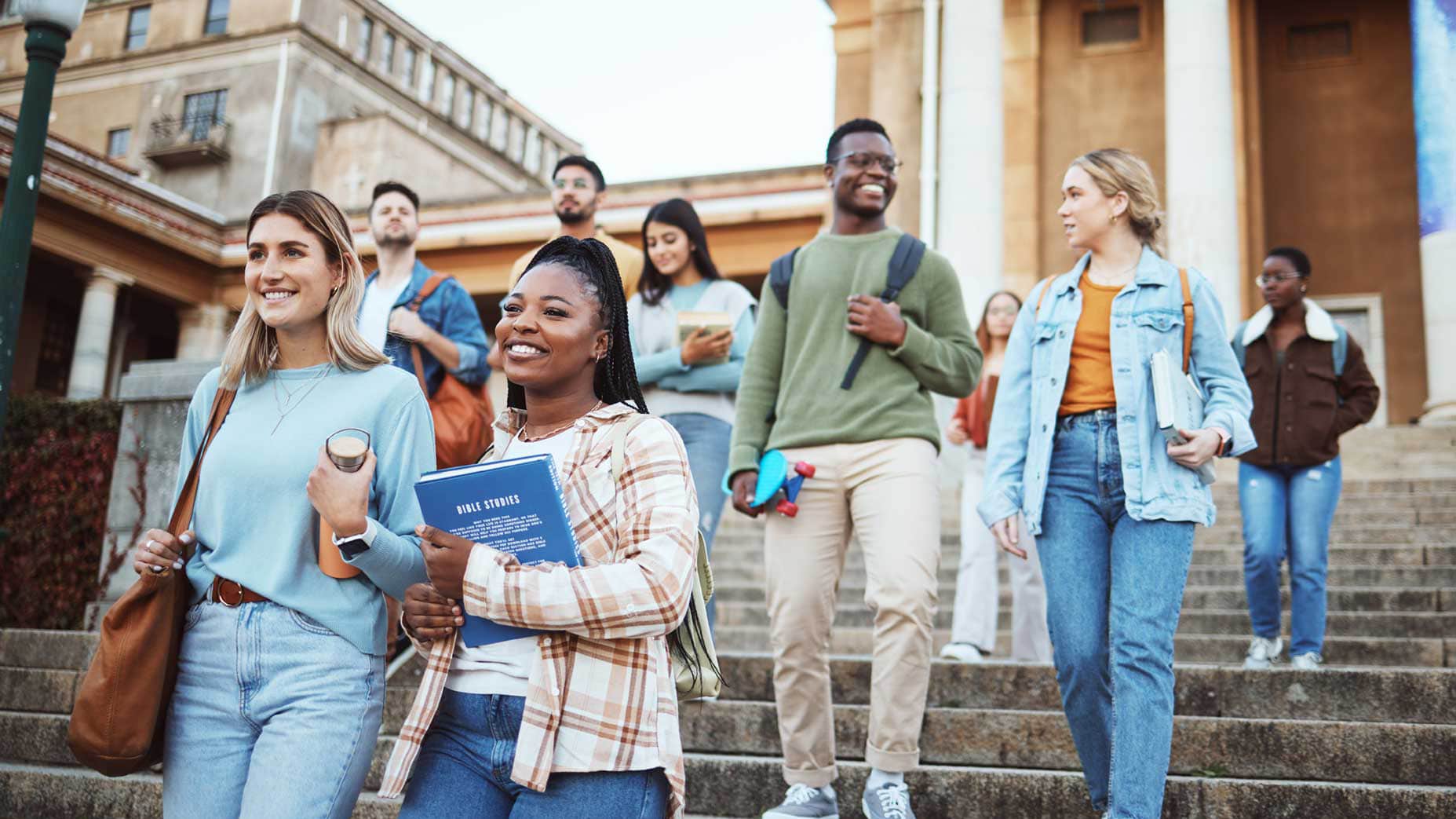 A group of smiling college students walking down the steps of a campus building, carrying books and backpacks. This vibrant scene highlights the journey of transfer students as they transition to a new college environment with confidence and excitement.