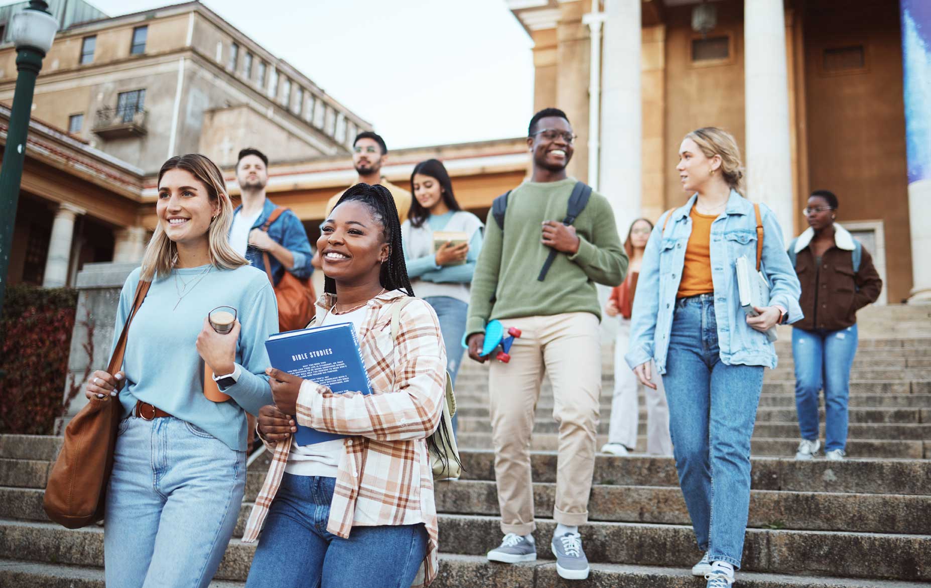 A group of smiling college students walking down the steps of a campus building, carrying books and backpacks. This vibrant scene highlights the journey of transfer students as they transition to a new college environment with confidence and excitement.