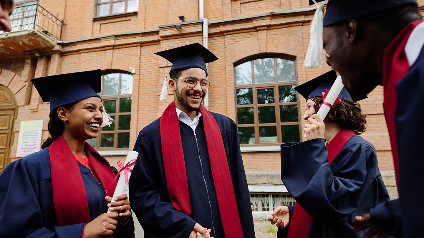 A group of smiling graduates in caps and gowns celebrating outdoors, holding diplomas. Their joy and achievement capture the culmination of their grad school journey, marking an important milestone in their advanced education.