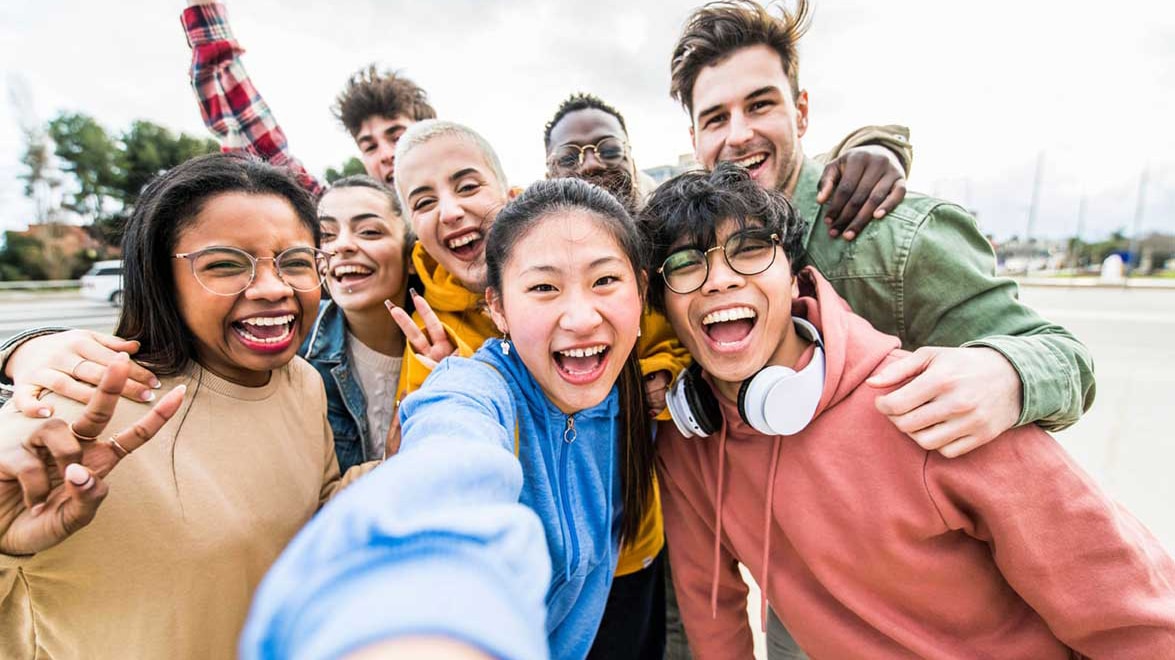 A group of diverse, smiling college students taking a joyful selfie outdoors. Their multicultural background and shared excitement reflect the vibrant experiences of international students as they build friendships and navigate college life together.