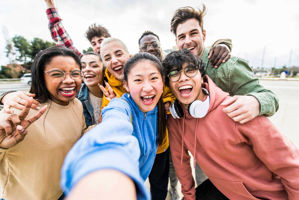 A group of diverse, smiling college students taking a joyful selfie outdoors. Their multicultural background and shared excitement reflect the vibrant experiences of international students as they build friendships and navigate college life together.